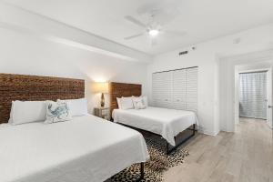two beds in a bedroom with white walls and wood floors at Beach Colony West 1C in Pensacola +44 photos