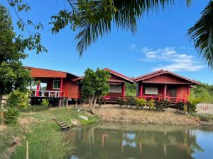 una casa rossa con un laghetto davanti di IngTawan Resort อิงตะวัน รีสอร์ท a Sing Buri