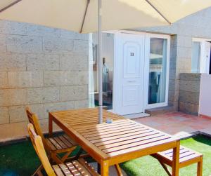 a wooden table with two chairs and an umbrella at Casita Playa Castillo "Vivienda 3B" in Caleta De Fuste