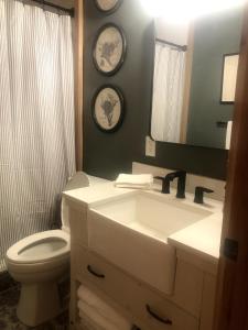 a bathroom with a sink and a toilet and two clocks at Adirondack Cabin in Schroon Lake