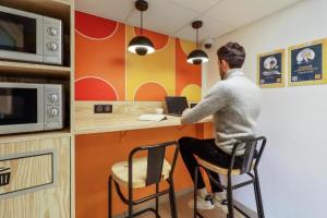 a man sitting at a kitchen counter with a laptop at Issy Citea Access dayuse Room - Work and Day Rest Timeshare -- 2 min tram - Formule Temps Partagé -- Navette ile d'Issy Avenue Paris 92320 espace nuit in Issy-les-Moulineaux