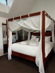 a bedroom with a canopy bed with white sheets at Gallery Walk Chalets - Tamborine Mountain in Mount Tamborine