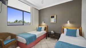 a room with two beds and a chair and a window at Ocean Parade 16 - Sleeps 4, Pool, Steps To Beach, Cafes in Coffs Harbour