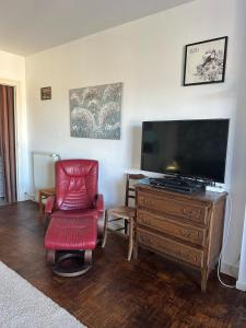 un salon avec une télévision et un fauteuil rouge dans l'établissement Maison de village proche du Lac de Vassivière, à Peyrat-le-Château