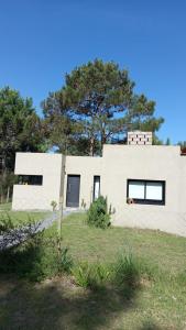 una casa blanca con un árbol en el fondo en Casa con Patio y Parrilla Zona Golf, en Villa Gesell