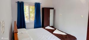 a bedroom with a bed with blue curtains and a window at Bele Beach Front Inn in Gokarna