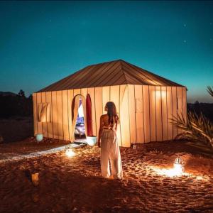 a woman standing in front of a tent with lights at Merzouga Desert Campsite &Activities in Merzouga