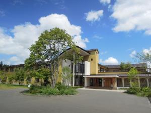 a yellow building with a tree in a parking lot at Hotel Folkloro Hanamakitowa in Hanamaki