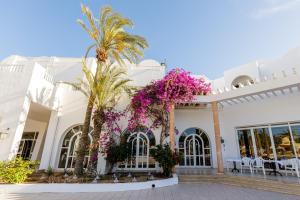 a white building with palm trees and purple flowers at Iris Hotel & Thalasso in Taguermess