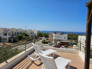 zwei weiße Stühle auf einem Balkon mit Blick auf eine Stadt in der Unterkunft Tranquil Penthouse Apartment Turtle Bay Village Esentepe in Ayios Yeoryios