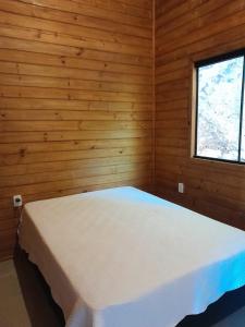 a white bed in a wooden room with a window at Residencial Bambu in Garopaba