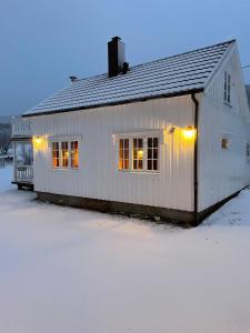 ein weißes Haus mit Lichtern im Schnee in der Unterkunft Marvelous farmhouse with amazing fjord and mountain view in Northern Norway in Nordøya