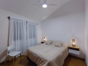 a white bedroom with a bed and a chair at Casa con pileta cómoda y equipada in Villa Carlos Paz
