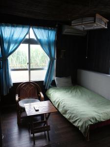 a bedroom with a bed and a table and a window at Guest House Miyakojima in Miyako-jima