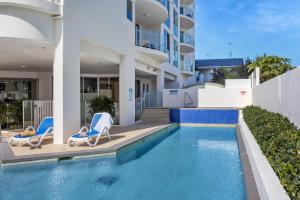 a swimming pool with two chairs and a building at Aqua Vista Resort in Maroochydore