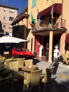メストレにあるホテル デッレ ローズの赤い車が乗る建物の前のテーブルと椅子