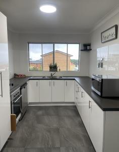 a white kitchen with white cabinets and a sink at Senior State Cup stay - Watch the Waves, Play the Game in Port Macquarie +6 photos