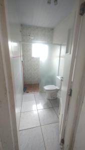 a white bathroom with a toilet and a window at Casa de temporada in Caraguatatuba
