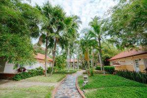 a walkway in front of a house with palm trees at Le Aqua Resort & Spa Phan Thiet - Swiss Village Resort & Spa in Mui Ne