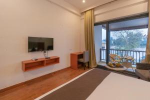 兰纳加Vanashraya Corbett Resort的一间卧室设有一张床、一台电视和一个阳台。