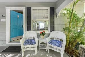 two wicker chairs and a table on a porch with a blue door at Orchid Suite in Key West