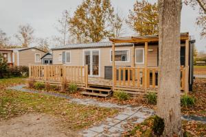 a manufactured home with a porch and a tree at Chalet Trigano 1-6 pers- 3 slaapk- 2 badk- Berging- Inchecken al vanaf 13 uur incl gebruik koffie en thee in Lauwersoog
