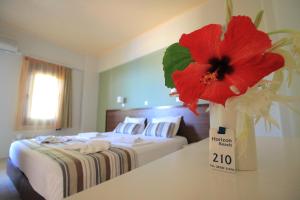a room with a bed with a red flower in a vase at Horizon Beach Hotel in Plakias
