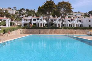 a large blue swimming pool with houses in the background at Ca'n Pekos Apartamento en la playa de Son Bou in Son Bou