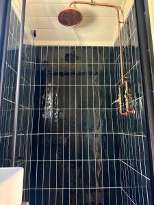 a bathroom with a shower with a black tiled wall at 'Bramley' Hut on private farm in Charsfield
