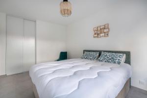 a white bedroom with a large white bed with blue pillows at Appartement pour 4 à 150m de la Mer in Sainte-Marie