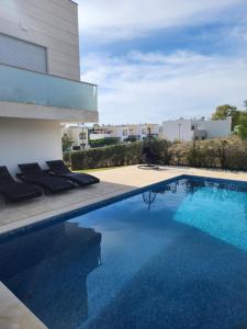 a swimming pool with chairs next to a building at Casa Rogel by Armação de Pêra with Heated Pool and Games Room in Alcantarilha