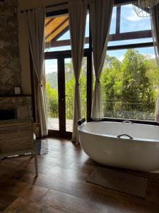 a bath tub in a room with a large window at Reserva Mauá chalés in Visconde De Maua
