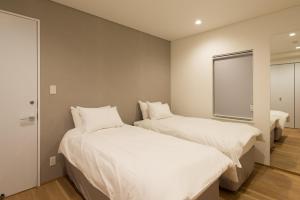 two beds in a room with white sheets and a window at Yuzuki in Kutchan