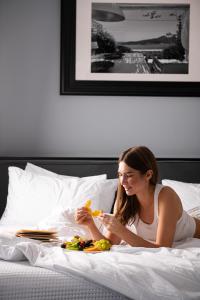 a woman laying in bed with a book and fruits at Athenian Riviera Hotel& Suites in Athens