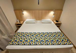 a bedroom with a large bed with a yellow and blue blanket at Hotel Rainha dos Apóstolos in Aparecida