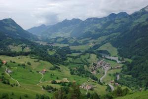 a green valley with a village in the mountains at Maison d'hôtes de la Gare in Montbovon