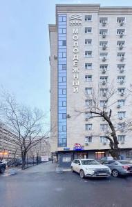 Un gran edificio con coches aparcados delante. en Eastern style apartment in Golden Square!, en Almaty