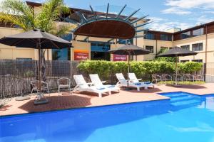 a pool with chairs and umbrellas next to a building at Heartland Hotel Auckland Airport in Auckland