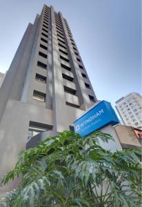 a tall building with a blue sign in front of a tree at Wyndham São Paulo Paulista in Sao Paulo +1 photo