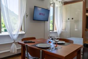 mesa de comedor con copas de vino y TV en la pared en Vista Lago-Appartamento Giardino dell'Eden, en Ghirla