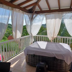a bed on a balcony with white drapes at villa timokei piscine et jacuzzi in Fond Saint-Jacques