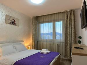 a bedroom with a bed with a purple blanket and a window at Luxury Glam Apartments Coresi Mall Area in Braşov