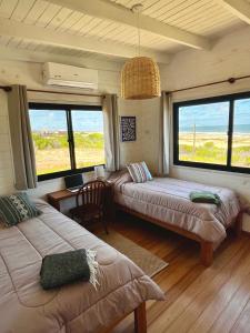 a room with two beds and a desk and windows at Casa Grande Punta del Diablo in Punta Del Diablo