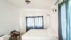 a white bedroom with a bed and a chair at Golden Sunset House in Acajutla