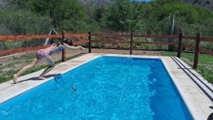 a woman is jumping into a swimming pool at CABAÑAS KUME in Potrero de los Funes