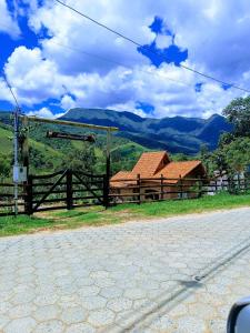 une maison en bois avec une clôture et des montagnes en arrière-plan dans l'établissement Rancho Pedacinho de Coração, à Itamonte