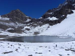 una persona parada en una montaña cubierta de nieve con un lago en Portezuelo del Viento - Hostel de Montaña en Las Cuevas