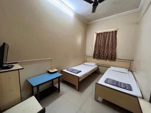 a small room with two beds and a television at Milan Guest House in Mumbai