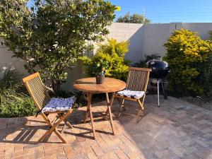 een houten tafel, 2 stoelen en een grill bij Cozy Cottage in Kaapstad