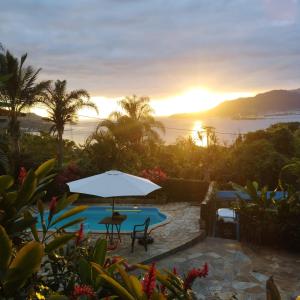 a pool with an umbrella and a sunset in the background at Suíte Vista Azul in Ilhabela